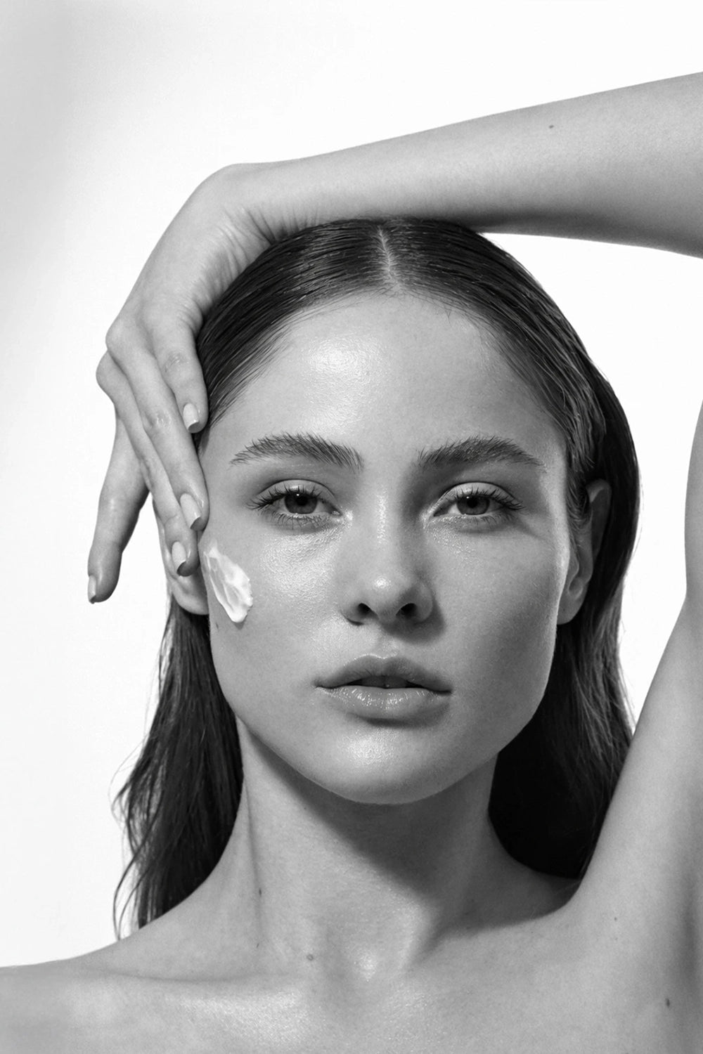 Black and white photo of a woman applying THAT CREAM with peptides to her face with a hand.
